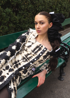 Woman sitting on a bench wearing a patterned dresss with a large black scrunchies in her hair.