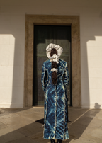 Person wearing a blue patterned dress and white scrunchie standing in front of a door.