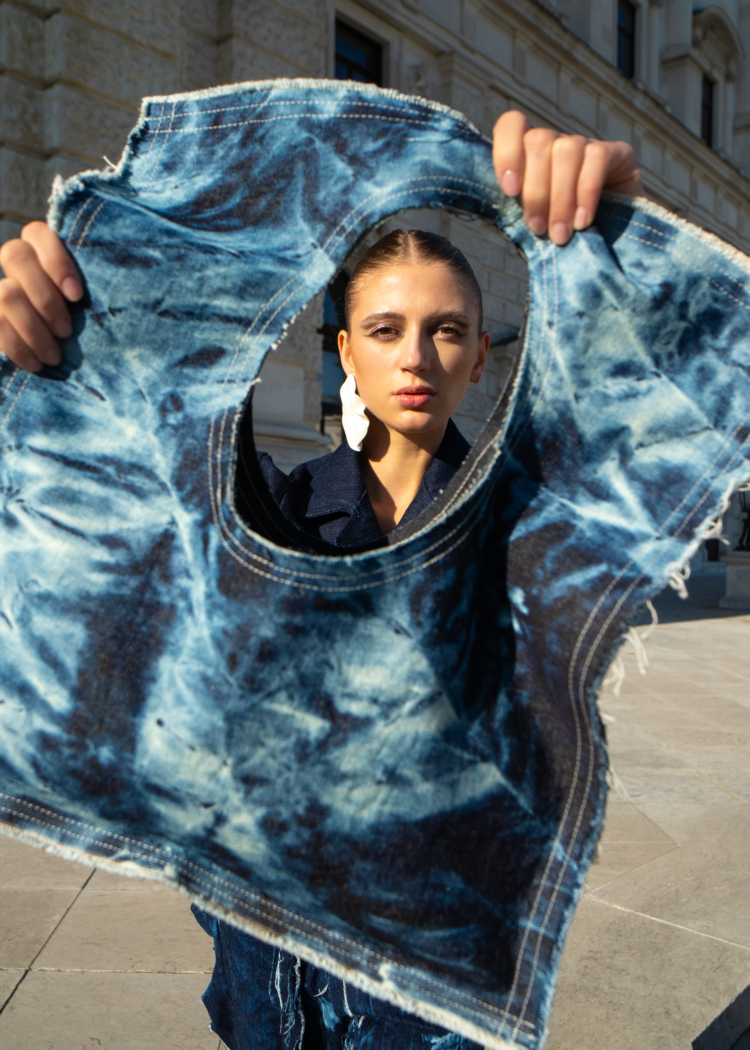 Person holding a &TIMELESS distressed denim tote bag, revealing a building in the background.